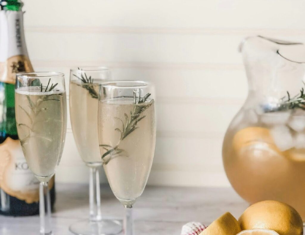 Champagne flutes with rosemary, bottle, pitcher, lemons. Elegant cocktail setup for a celebration.