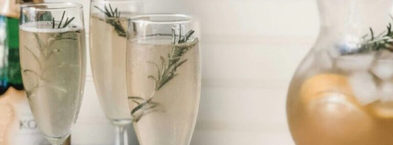 Champagne flutes with rosemary, bottle, pitcher, lemons. Elegant cocktail setup for a celebration.